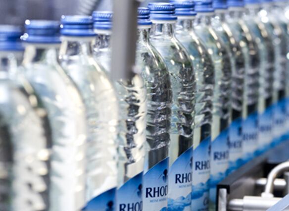Viele Glasflaschen stehen in einer Produktionsreihe nebeneinander. Alle haben blaue Deckel und blaue Etiketten.