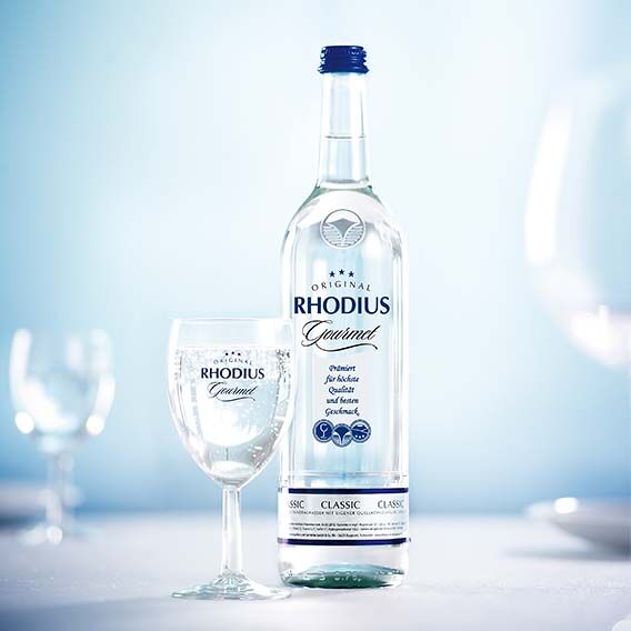 Eine Flasche Rhodius Gourmet steht mit drei Gläsern auf einem Tisch.