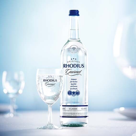 A bottle of Rhodius Gourmet stands on a table with three glasses.