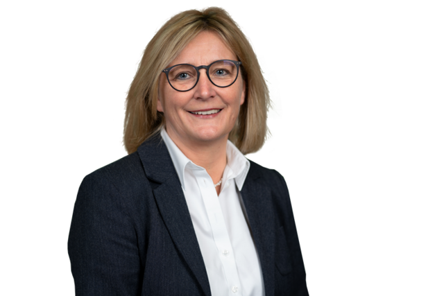 Woman with blond long hair wearing glasses and a white shirt and dark jacket looks into the camera and smiles.