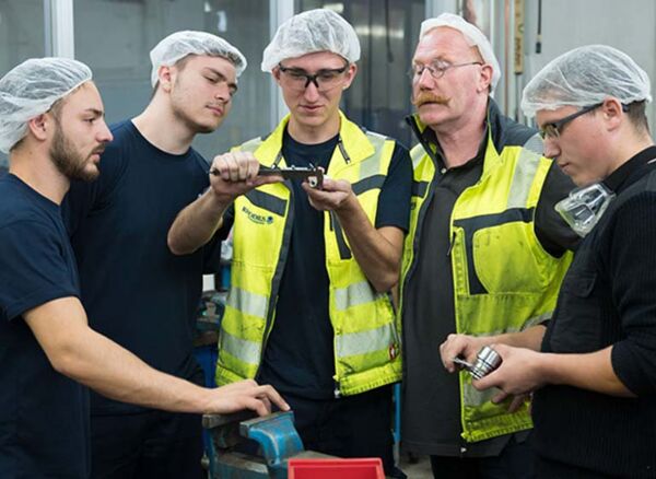 Mann in blauem Arbeitsoverall steht mit vor der Brust verschränkten Armen vor einer Anlage und blickt in die Kamera.